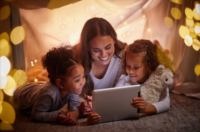 mother and children live streaming movies on tablet or digital kids app in a tent camping at night and bokeh lights care, love mom reading ebook to happy girl or online games with home wifi in dark