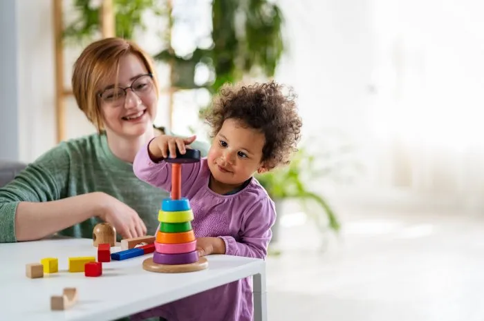 mother looking at a child playing with an educational didactic toy preschool teacher with a child playing with didactic toys mixed race family