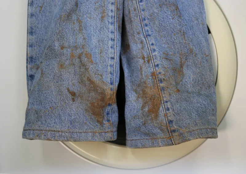 muddy jeans on a washing machine mud stain on jeans stained jeans before laundry the stain is metaphore for embarrassment, guilt, shame