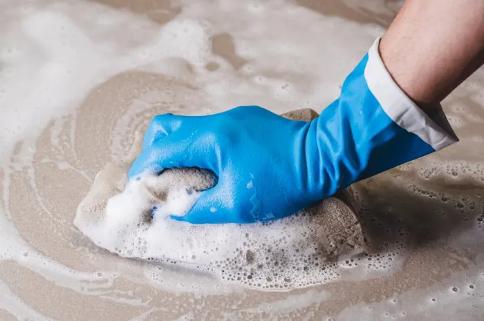 hand of man wearing blue rubber gloves is using a sponge cleaning the tile floor