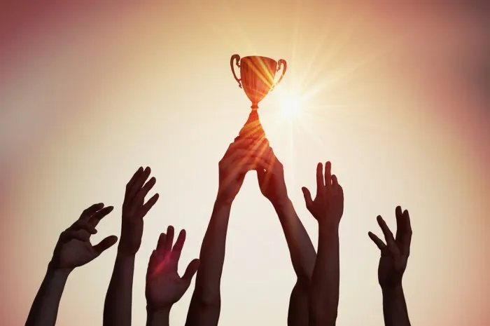 winning team is holding trophy in hands silhouettes of many hands in sunset