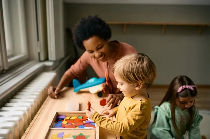 happy kid and his african american teacher using wooden puzzle shapes while playing at kindergarten