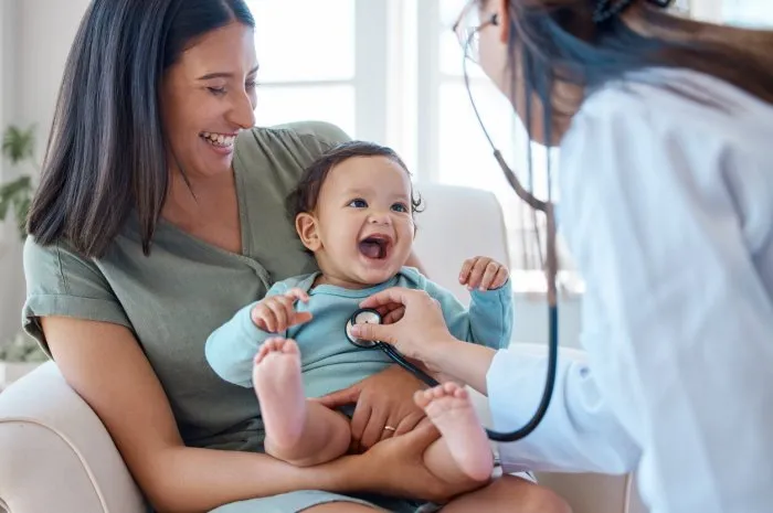 shot of a baby sitting on her mother's lap while being examined by a doctor
