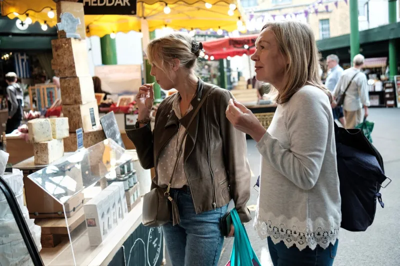 two senior women friends enjoying shopping cheese in a street market borough market, london