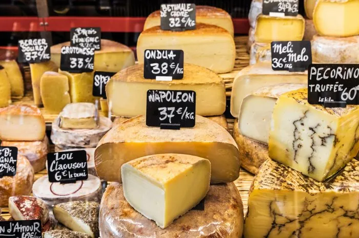 a large selection of different french and italian cheeses on the counter of a small store at the market in the bastille district paris, france