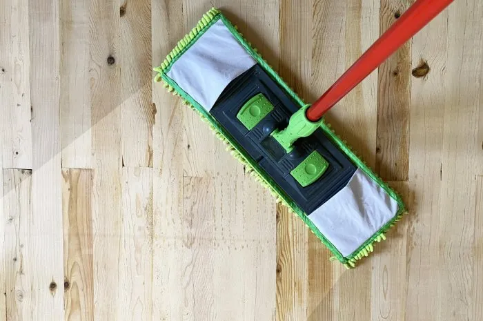 cleaning wooden floor with green mop in house or office, laminate floor top view