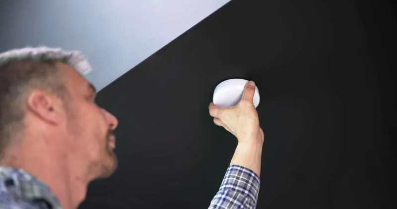 person's hand installing smoke detector on ceiling wall at home