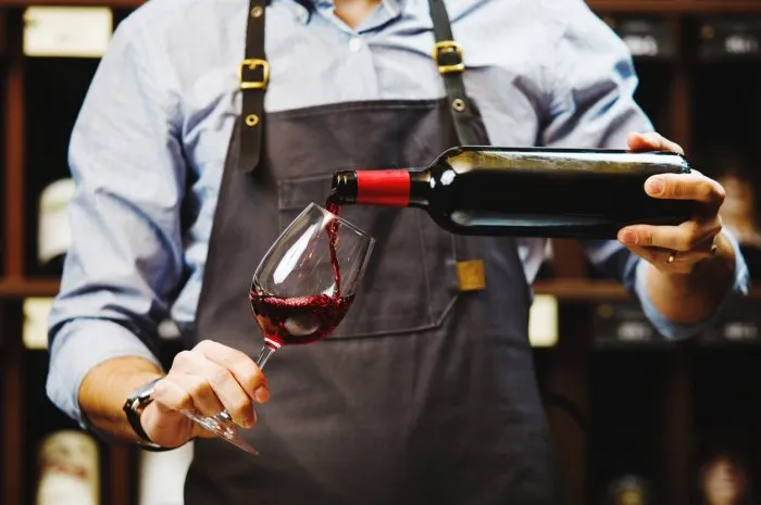 male sommelier pouring red wine into long-stemmed wineglasses waiter with bottle of alcohol beverage bartender at bar counter pour elite drink into long-stemmed glass