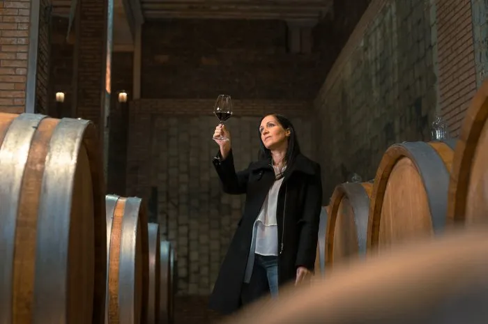 woman in the wine cellar with barrels in background drinking and tasting wine