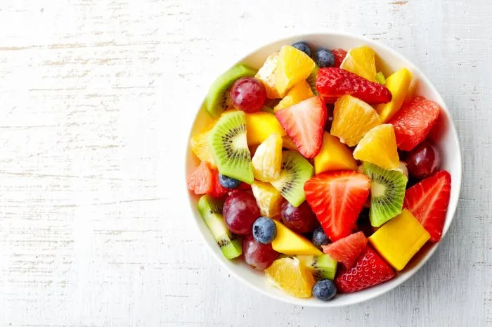 bowl of healthy fresh fruit salad on wooden background top view