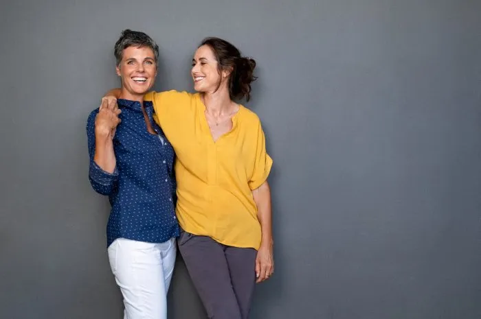mature happy women embracing each other against grey wall with copy space happy laughing ladies in smart casual standing on gray background cheerful middle aged woman with hand on shoulder of her stylish friend