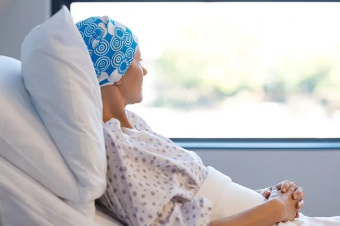 young woman in bed suffering from cancer thoughtful woman battling with tumor looking out of window young patient with blue headscarf recovery in hospital on bed