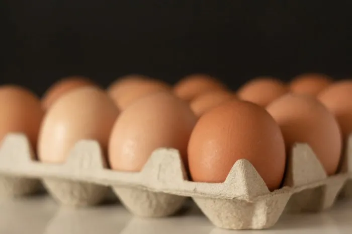 close up photo of a tray with eggs - a lot of brown eggs in a cardboard stand - on a white table and with a black background