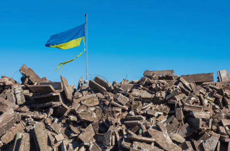 war in ukraine destroyed ukrainian building and damaged flag in the wind