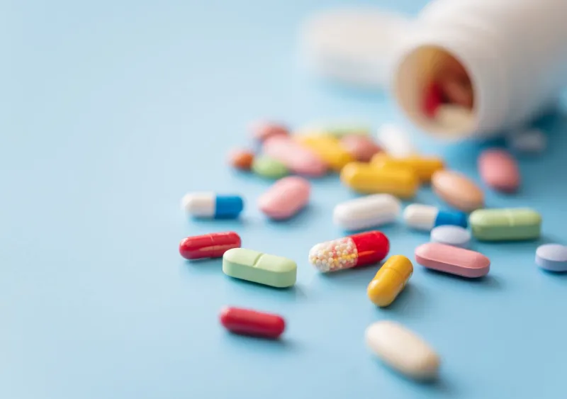 colorful pills scattered from white plastic pill bottle on blue background shallow dof
