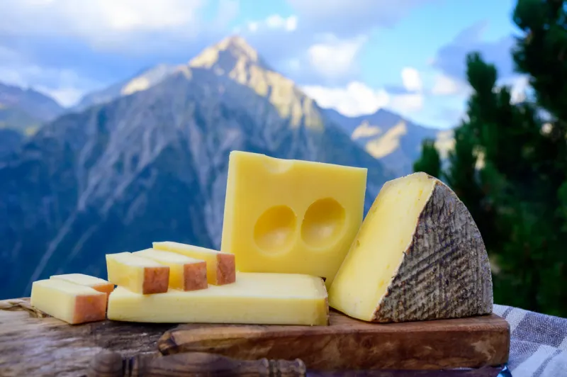 cheese collection, french beaufort, abondance, emmental, tomme de savoie cheeses served outdoor in savoy region, with alpine mountains peaks in summer on background