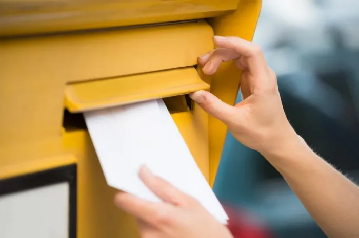 closeup of woman's hands inserting letter in mailbox