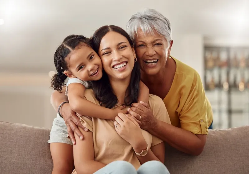 grandmother, mom and child hug in a portrait for mothers day on a house sofa as a happy family in colombia smile, mama and elderly woman love hugging young girl or kid and enjoying quality time