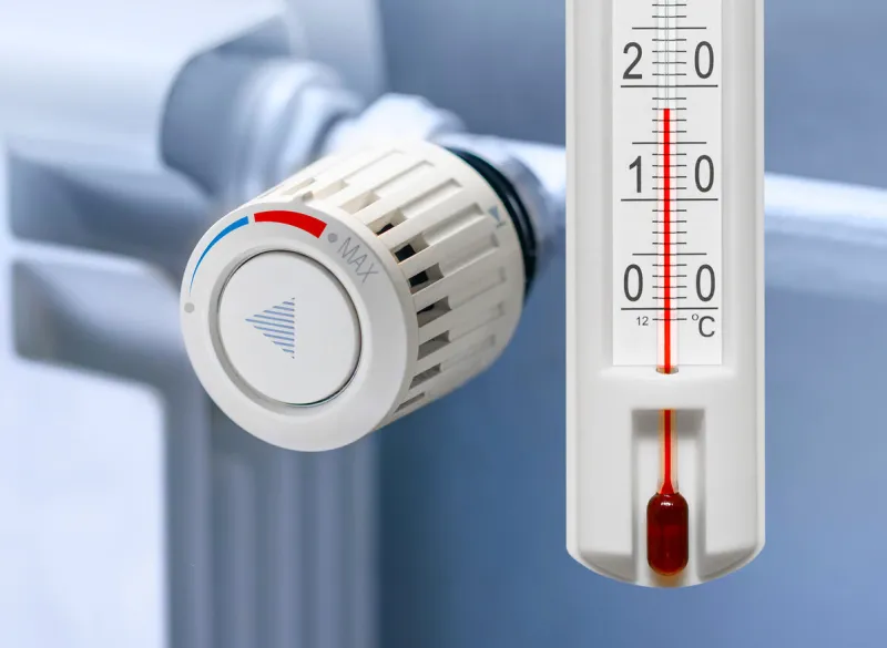 heating radiator thermostat set to low temperature and room thermometer for saving money at heating costs energy crisis, energy efficiency and rising heating costs in europe