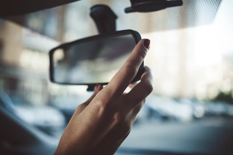 a man is driving a rear-view mirror in the car