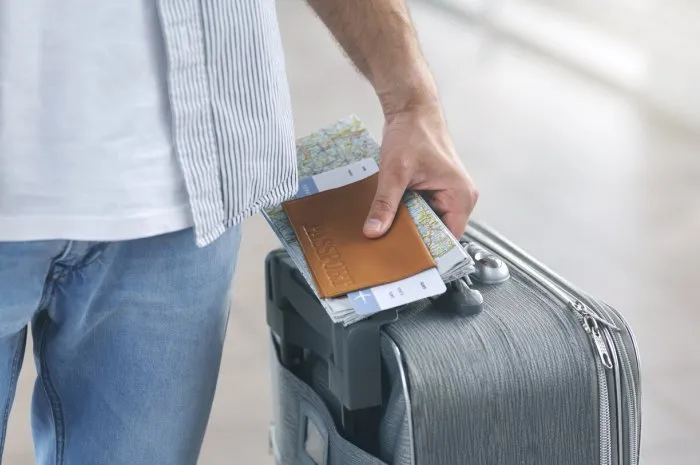 travelling concept man holding his passport and carrying suitcase, close up
