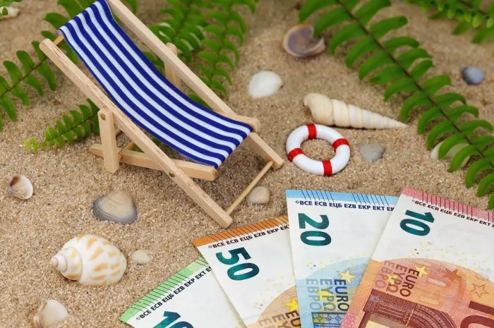 deck chair with euro banknotes in the sand with sea shells and tropical background, concept of saving money for a holiday trip or high vacation expenses