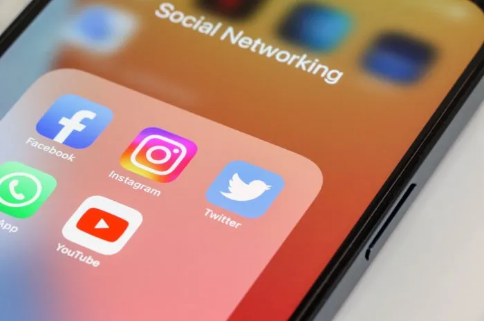 close-up of popular social media app icons, facebook, instagram, twitter, whatsapp and youtube, in that order, displayed on smartphone screen with orange wallpaper device is on white background