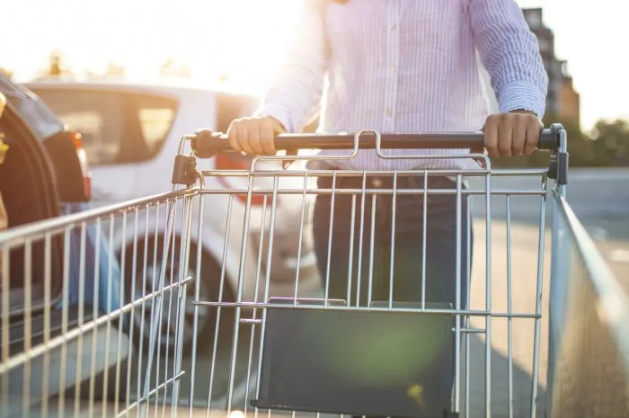 woman with bags and shopping cart loads a car woman putting bags into car after shopping woman pushing supermarket cart in urban public parking