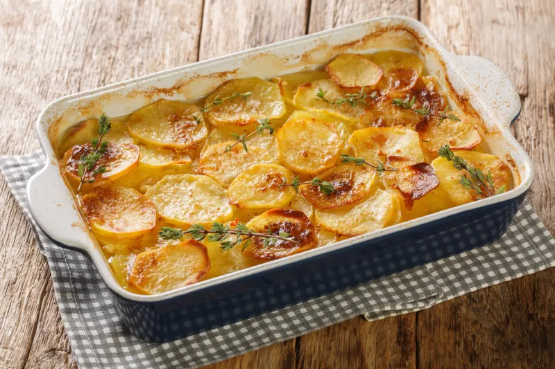 scalloped potatoes, potato casserole with the addition of herbs, onion and garlic in a ceramic baking dish closeup on the table horizontal
