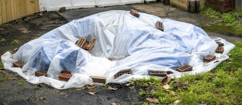 backyard garden debris covered with clear plastic cover and held down with bricks