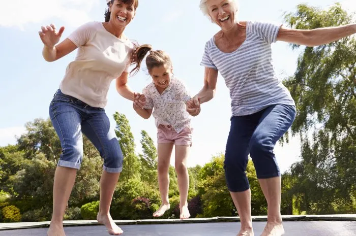 grandmother, granddaughter and mother bouncing on trampoline smiling to camera