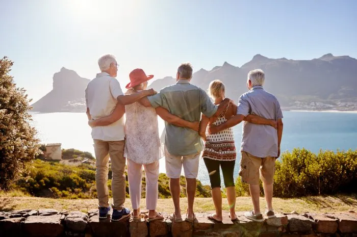 rear view of senior friends visiting tourist landmark on group vacation standing on wall