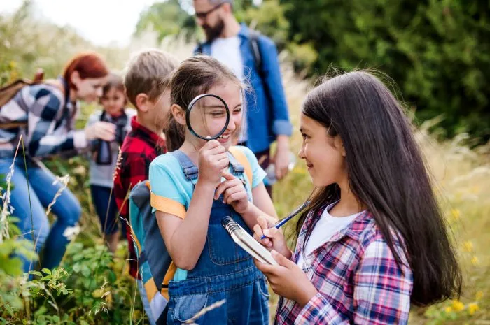 a group of small school children with teacher on field trip in nature, learning science