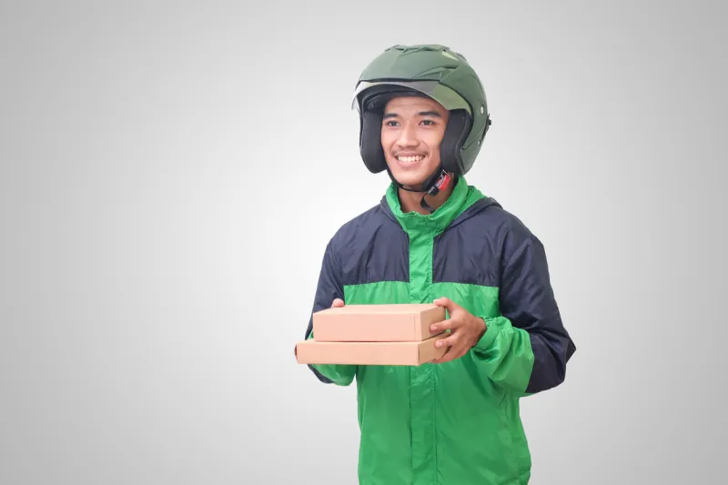 portrait of asian online courier driver wearing green jacket and helmet delivering package and box for customer isolated image on white background