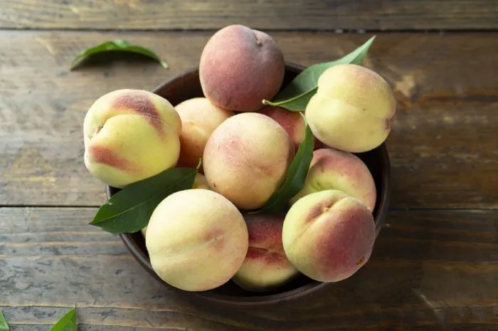 ripe peaches with leaves in a clay bowl on a wooden table fresh harvest