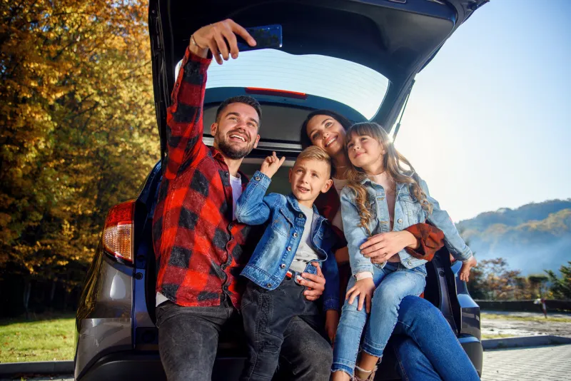 joyful happy stylish parents with their cute lovely children are making funny selfie on smart phone while sitting in the trunk happy modern family concept