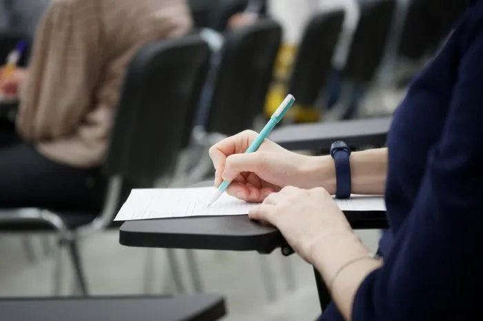 a girl writes a dictation or fills out documents in the audience, sitting on a school chair with a writing stand close-up no face
