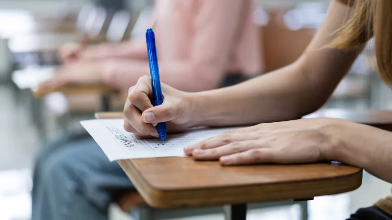 close up of young female university students concentrate on doing examination in the classroom girl student writes the answer of the examinations on the answer sheet in the classroom