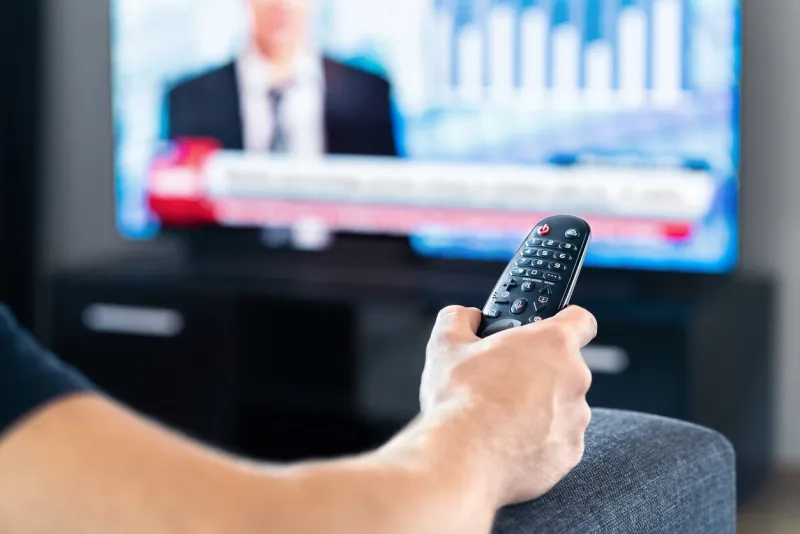 man watching tv news program and sitting on couch home television remote control in hand politics, business or finance network channel online live broadcast in monitor screen morning newscast