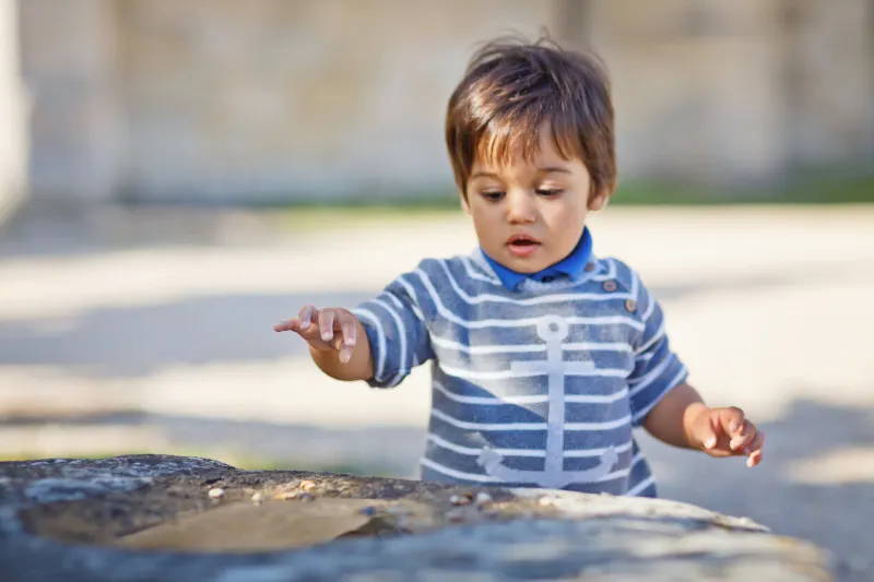 portrait of a little eastern handsome baby boy playing outdoor in the park arabian child fun on the street with small rocks in a puddle