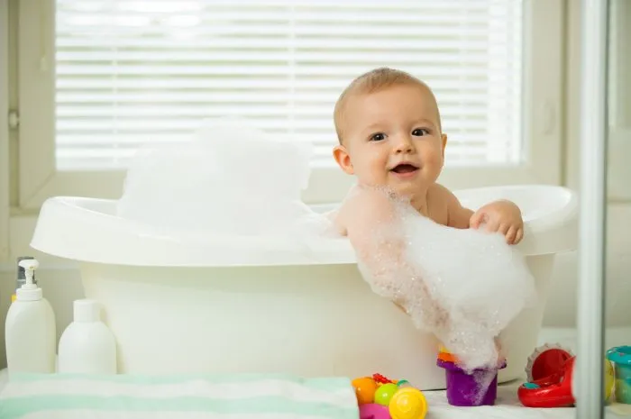 cute little baby sitting in white bathtub with foam and soap bubbles taking bath and playing with toys baby hygiene