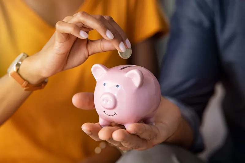 close up of man holding pink piggybank while woman putting coin in it indian young couple saving money for their wedding close up of woman hand putting euro money in piggy bank to save for the purchase of an house