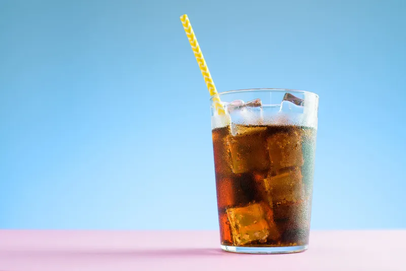 a glass of cola with ice cubes on blue and pink background