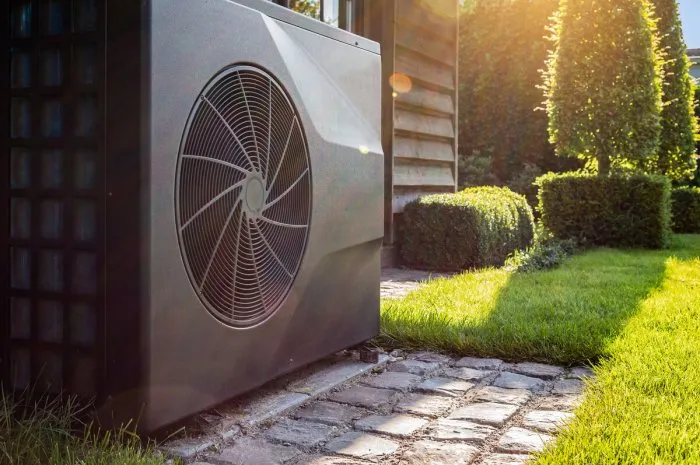 close-up of black full inverter heat pump outside in the garden, near wooden pool house on a sunny day lens flare on the image