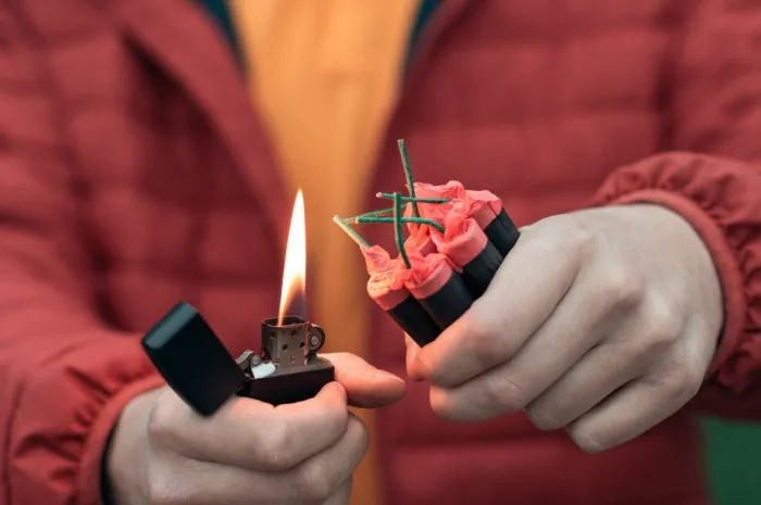 man in red jacked lighting up several firecrackers in his hand using gasoline lighter guy getting ready for new year fun with fireworks or pyrotechnic products