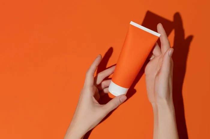 female hands holding blank orange plastic cosmetic tube on orange backgroundmockup high quality photo