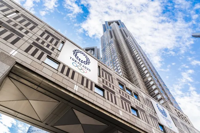 tokyo, japan - nov29 2017  2020 olympic concept - looking up view of tokyo metropolitan government building with tokyo 2020 olympic games logo, skyscrapers reflect dramatic blue sky