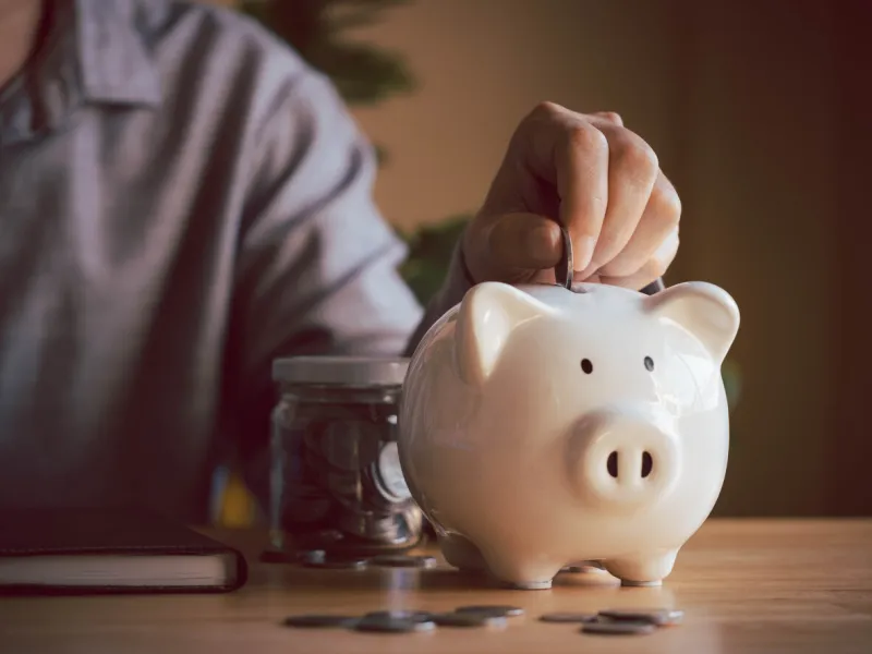 person hand put coin into white piggybank for money saving planning for future, investment, fund, and donation secure once retirement, plan for education money saving financial banking concept