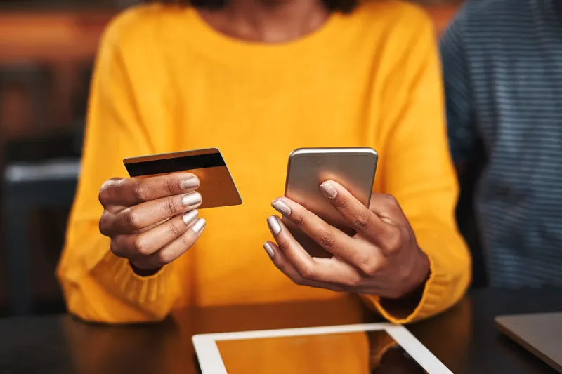 close-up of a young woman in cafeteria using mobile phone and credit card for shopping online
