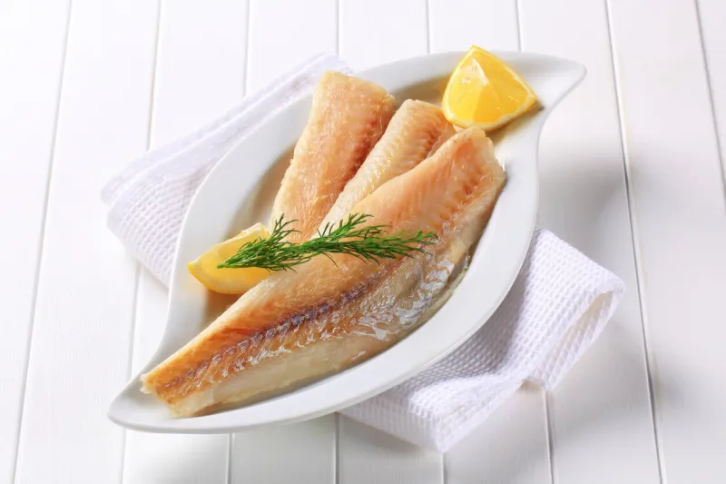 fish filets displayed on white plate with lemon and herbs